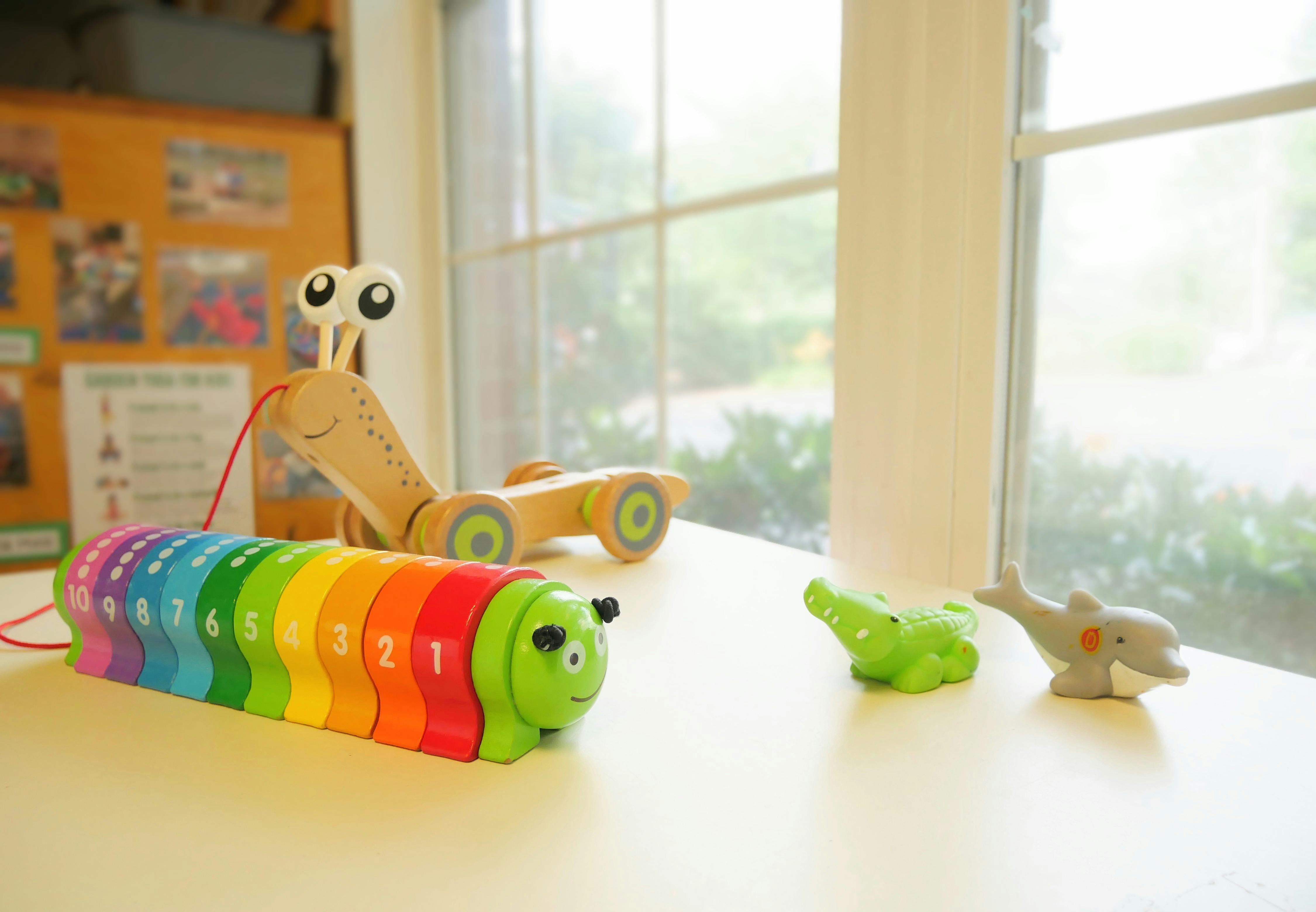 Rainbow caterpillar toy, wooden snail toy, and small animal figurines on a surface