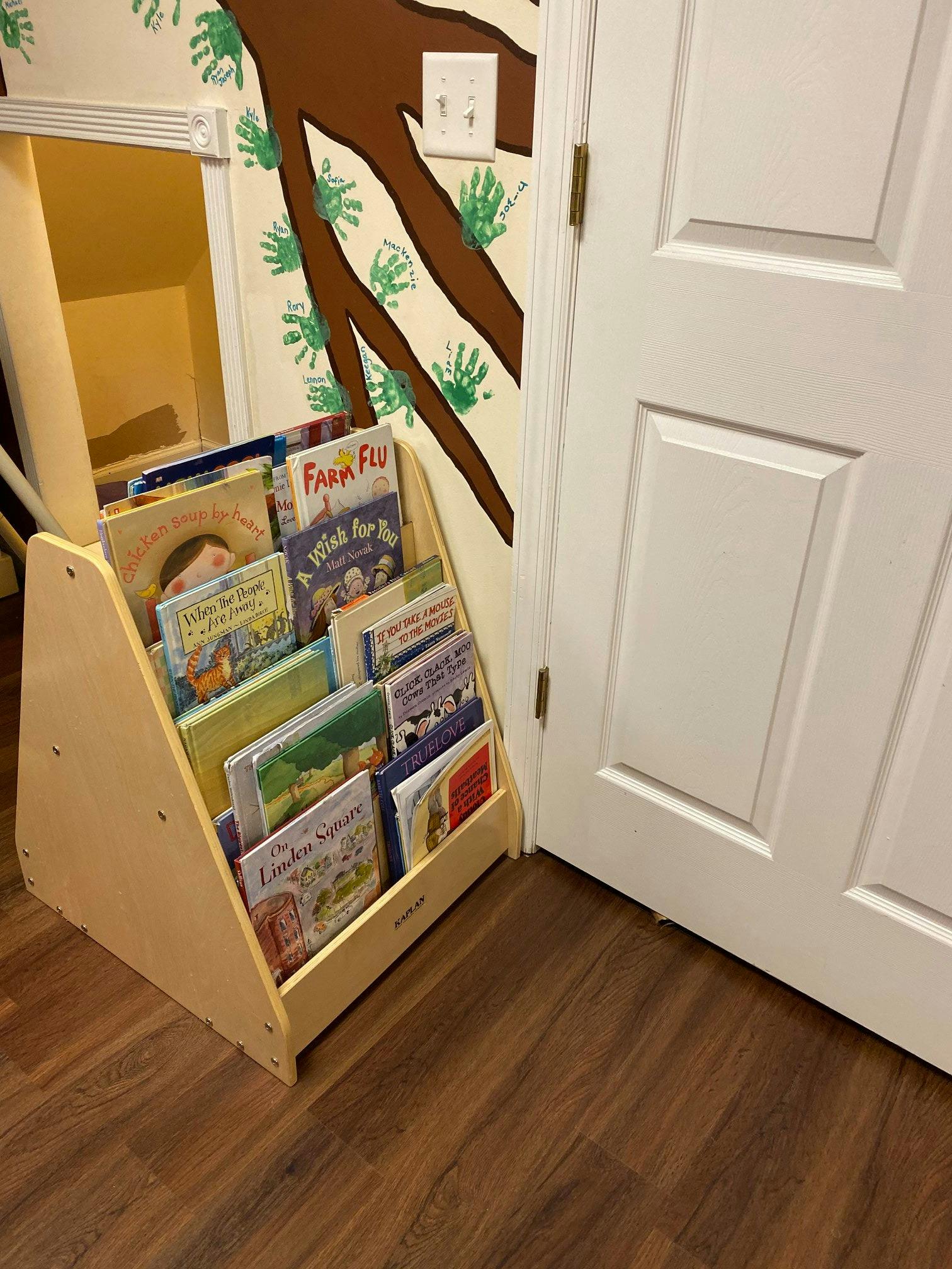 Children's books in a wooden display shelf next to a white door