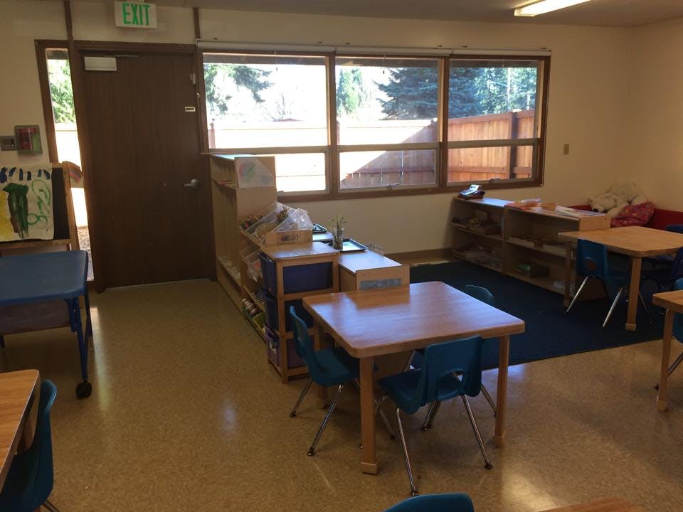Classroom with small tables and chairs, shelves, and large windows