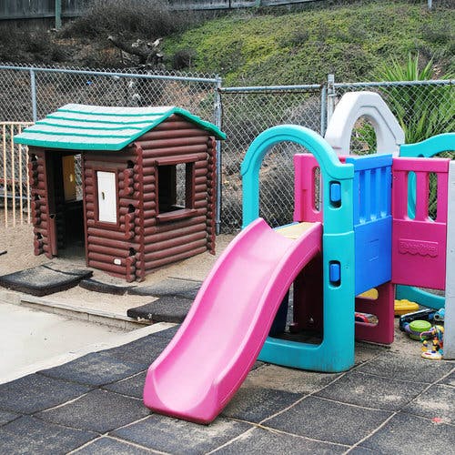 Playground with a small log cabin playhouse and a colorful slide structure