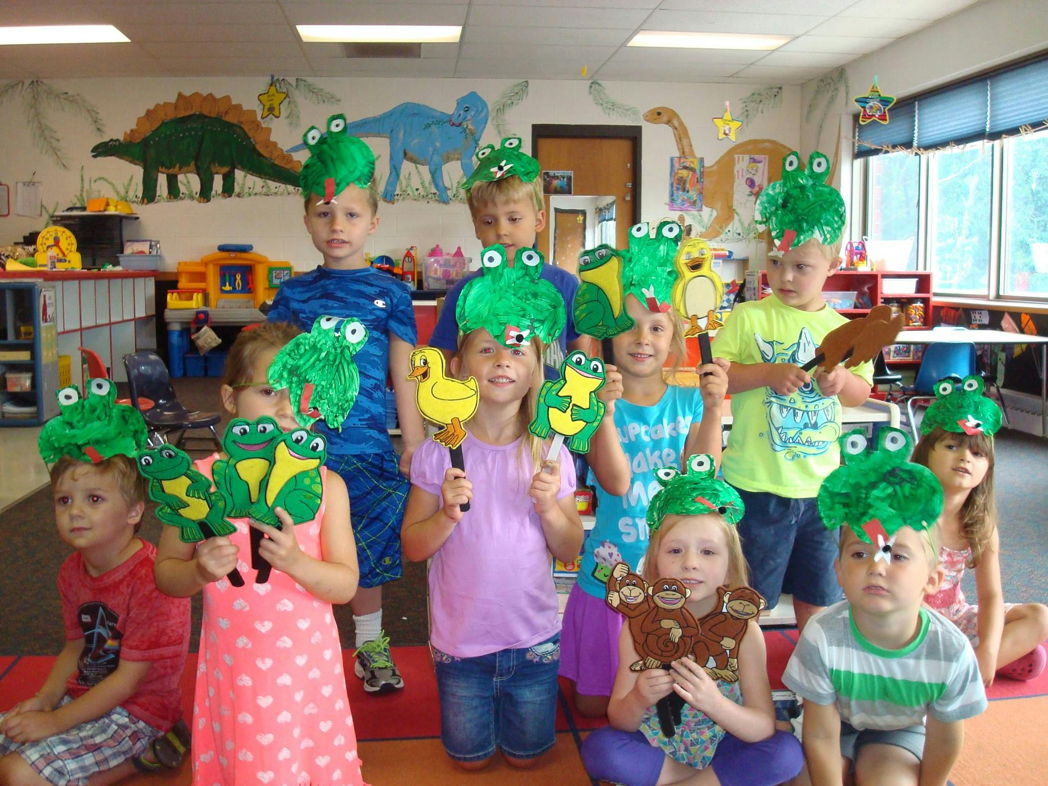 Children wearing frog hats and holding frog and duck puppets