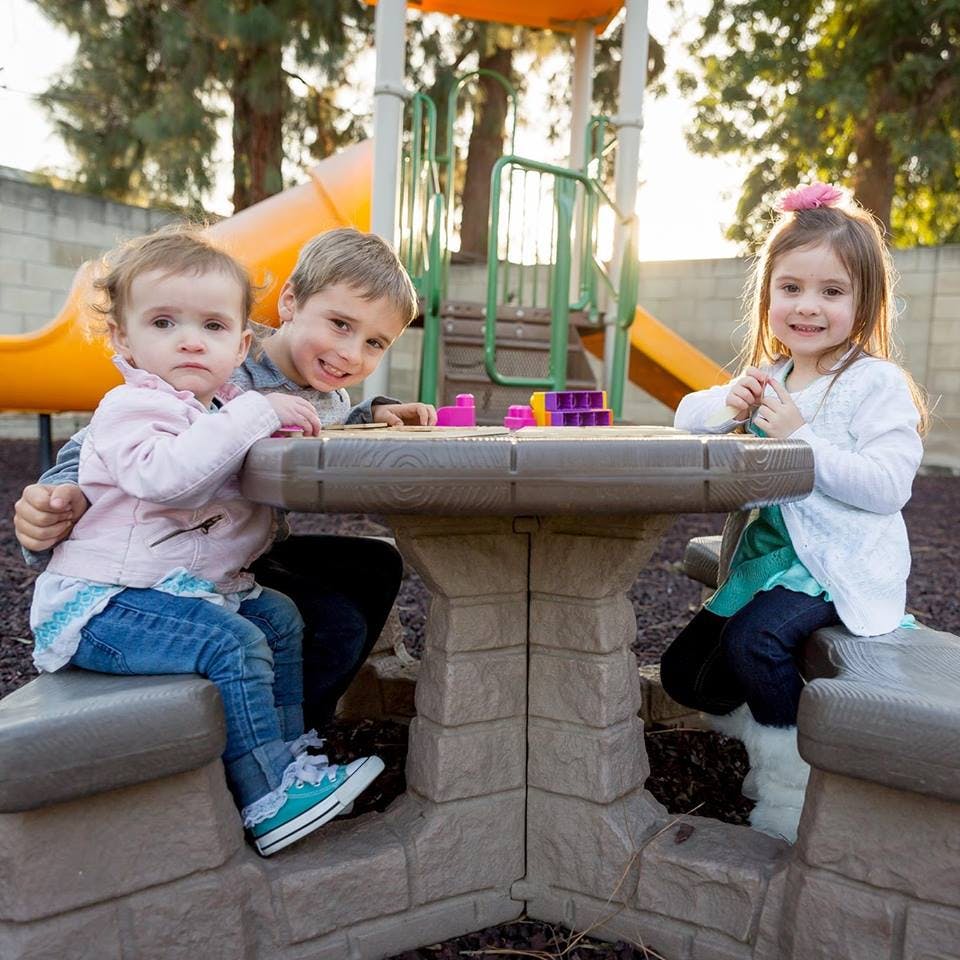 Three children sitting at a small table on a playground