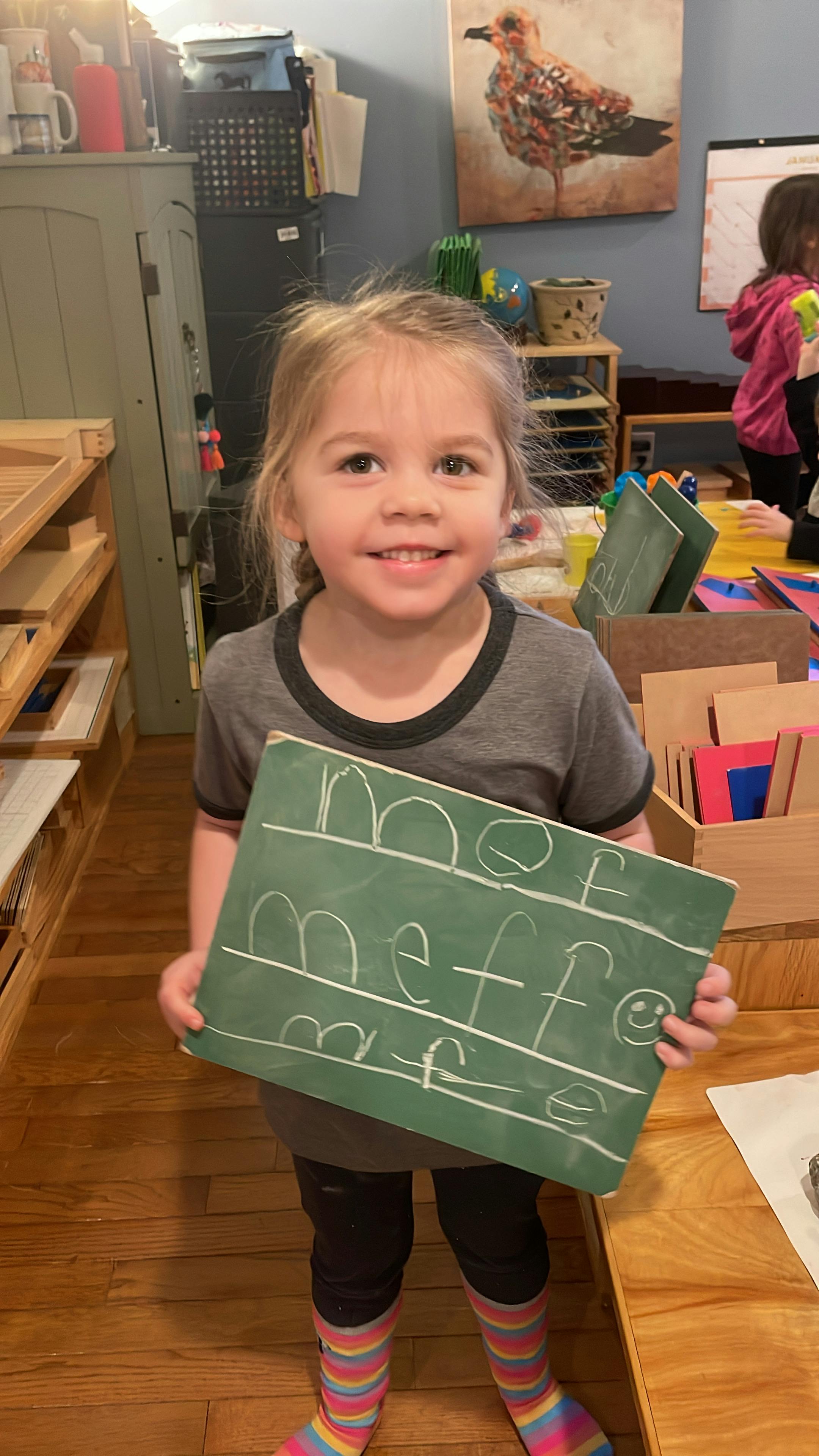 Child holding a small green chalkboard with white writing