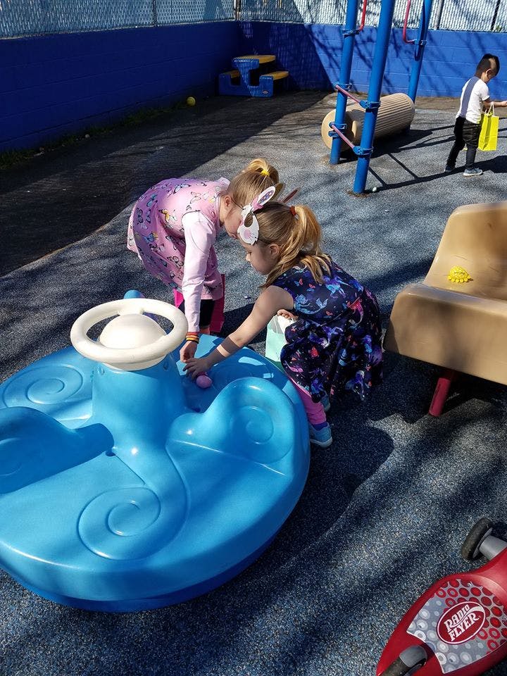 Two children playing with a blue toy car on a playground