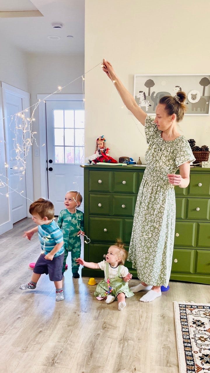 Person holding up string lights with three young children watching