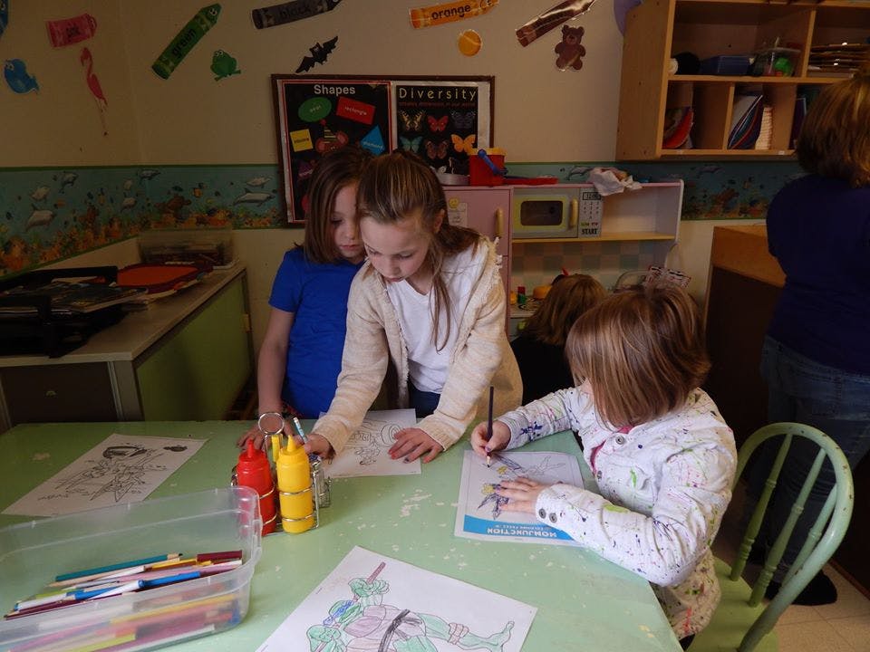 Three children drawing and coloring at a table in a classroom