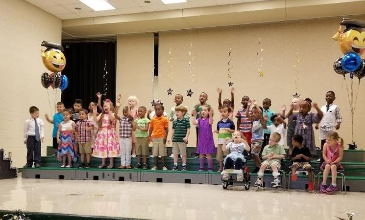 Group of children on a stage, some waving
