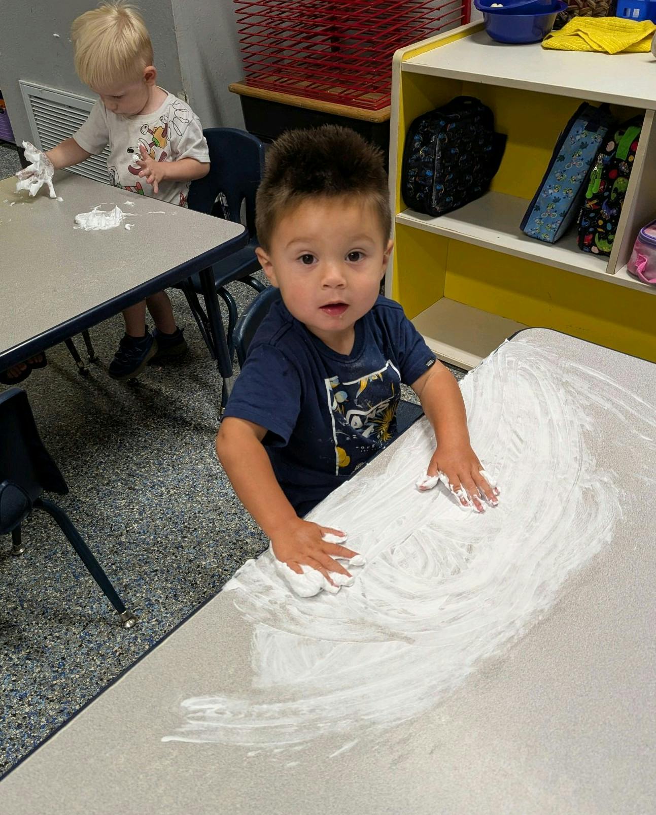Child playing with white foam on a table in a classroom