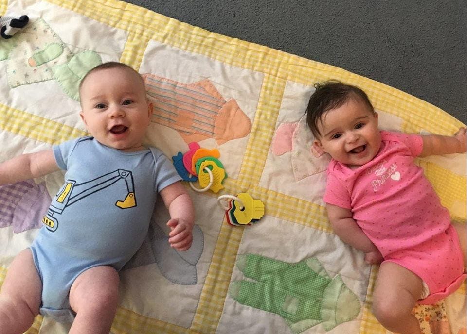 Two babies lying on a quilt with toys