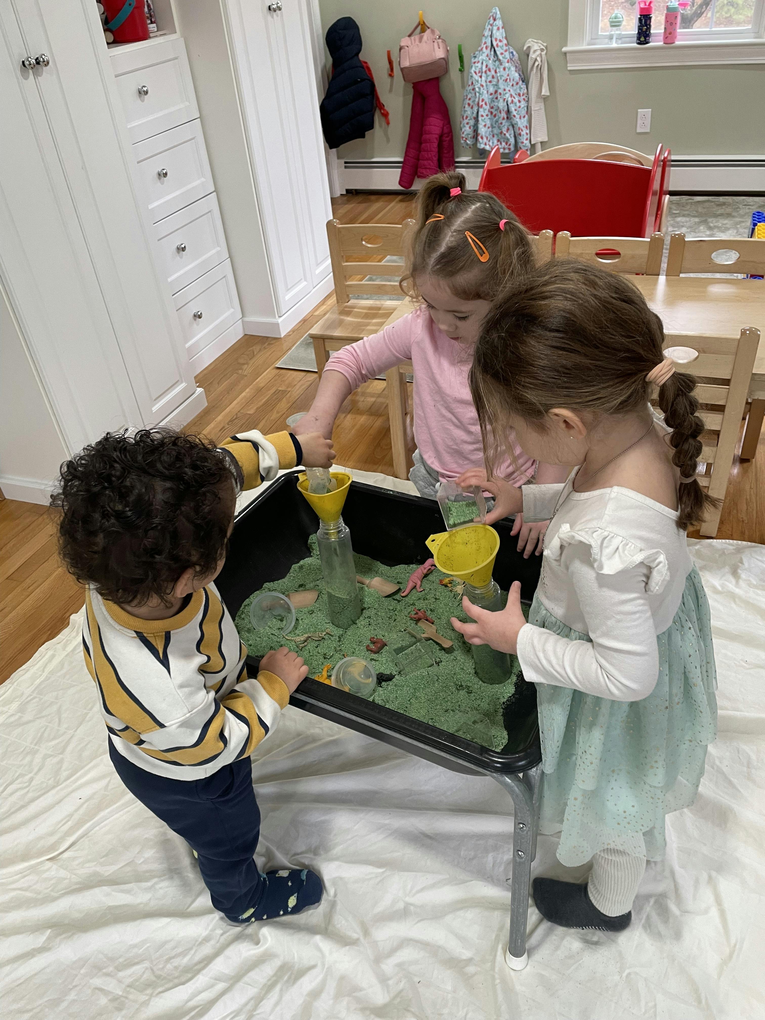 Three children playing with kinetic sand and toys at a table