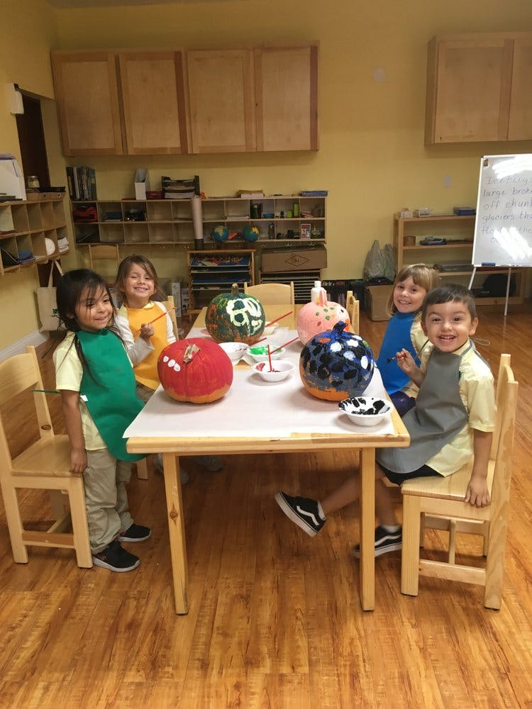 Children painting pumpkins at a table in a classroom