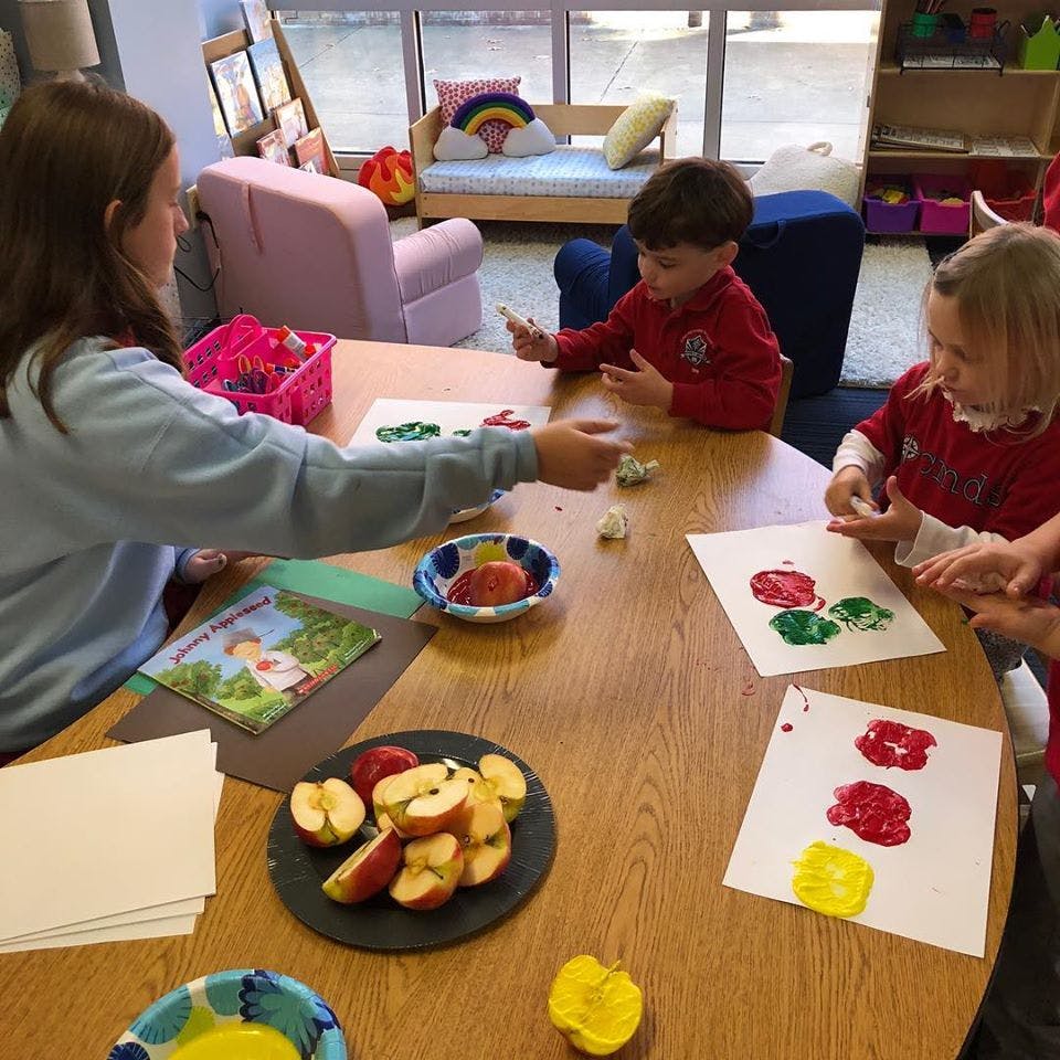 Person and two children doing apple stamping art at a table