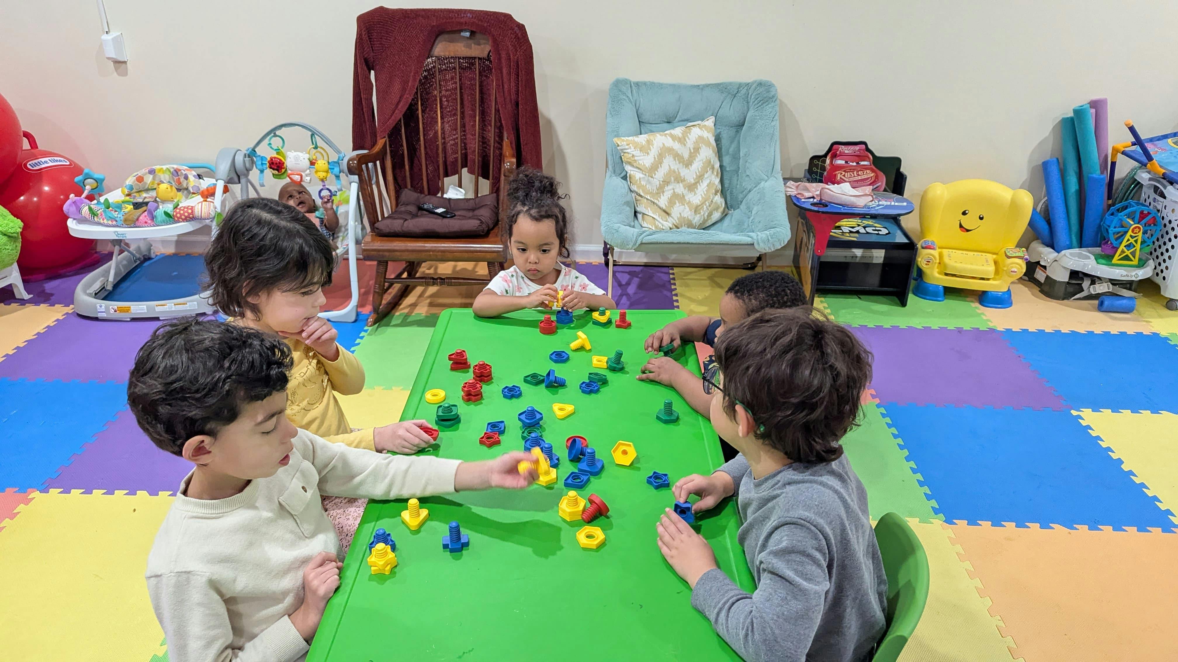 Children sitting at a green table playing with colorful plastic building blocks
