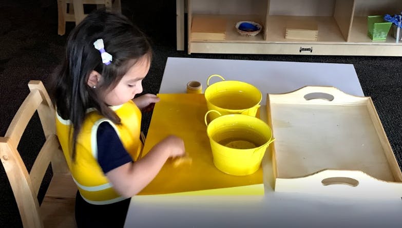 Child working at a table with yellow buckets and a tray