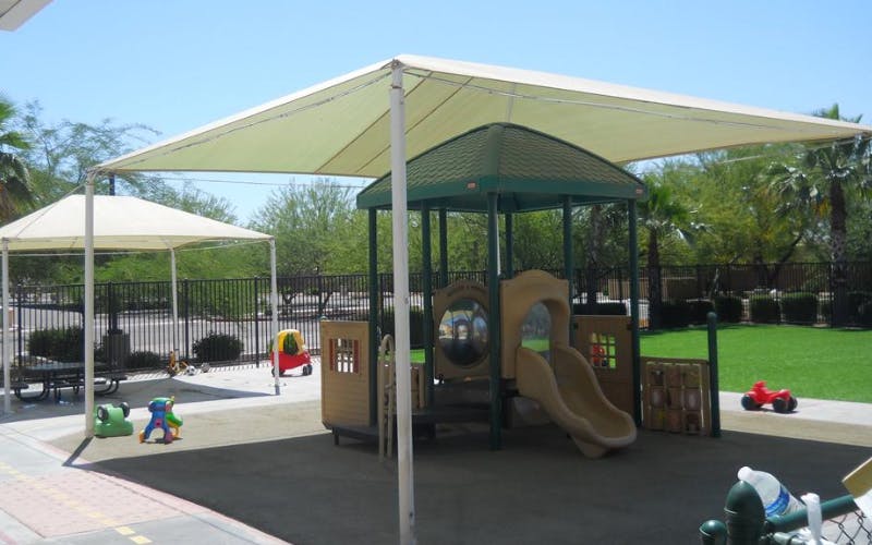 Outdoor playground area with a play structure, slide, and a shade cover