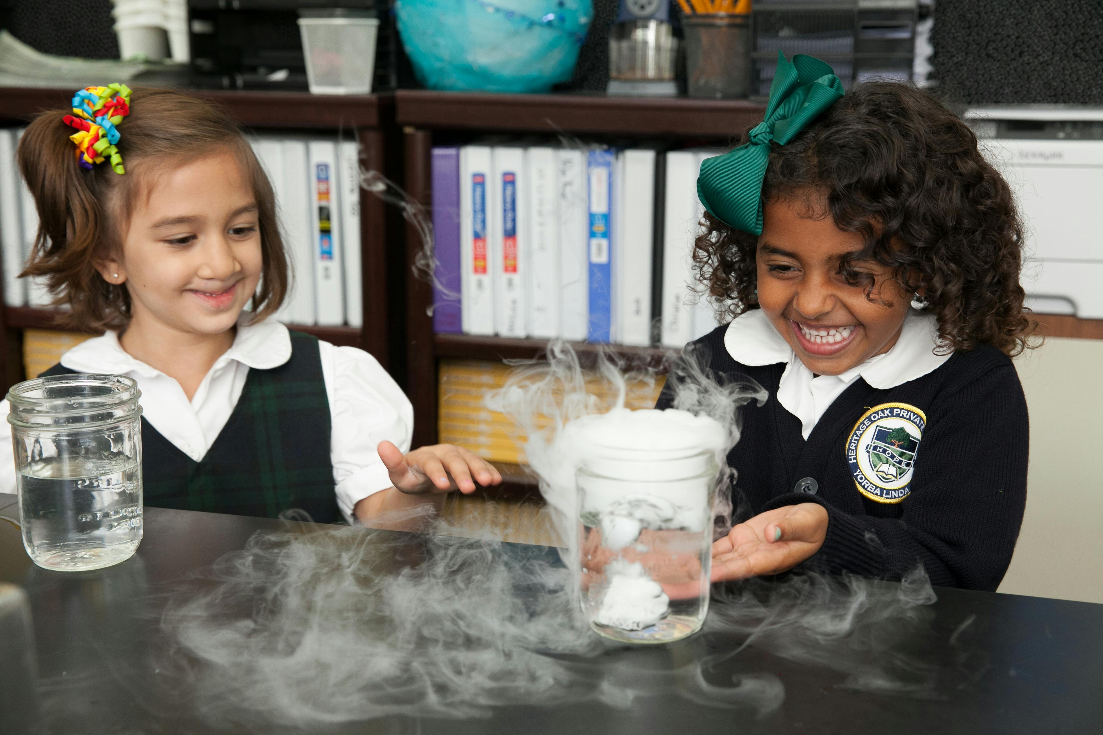 Two children watching a science experiment with smoke coming from a jar
