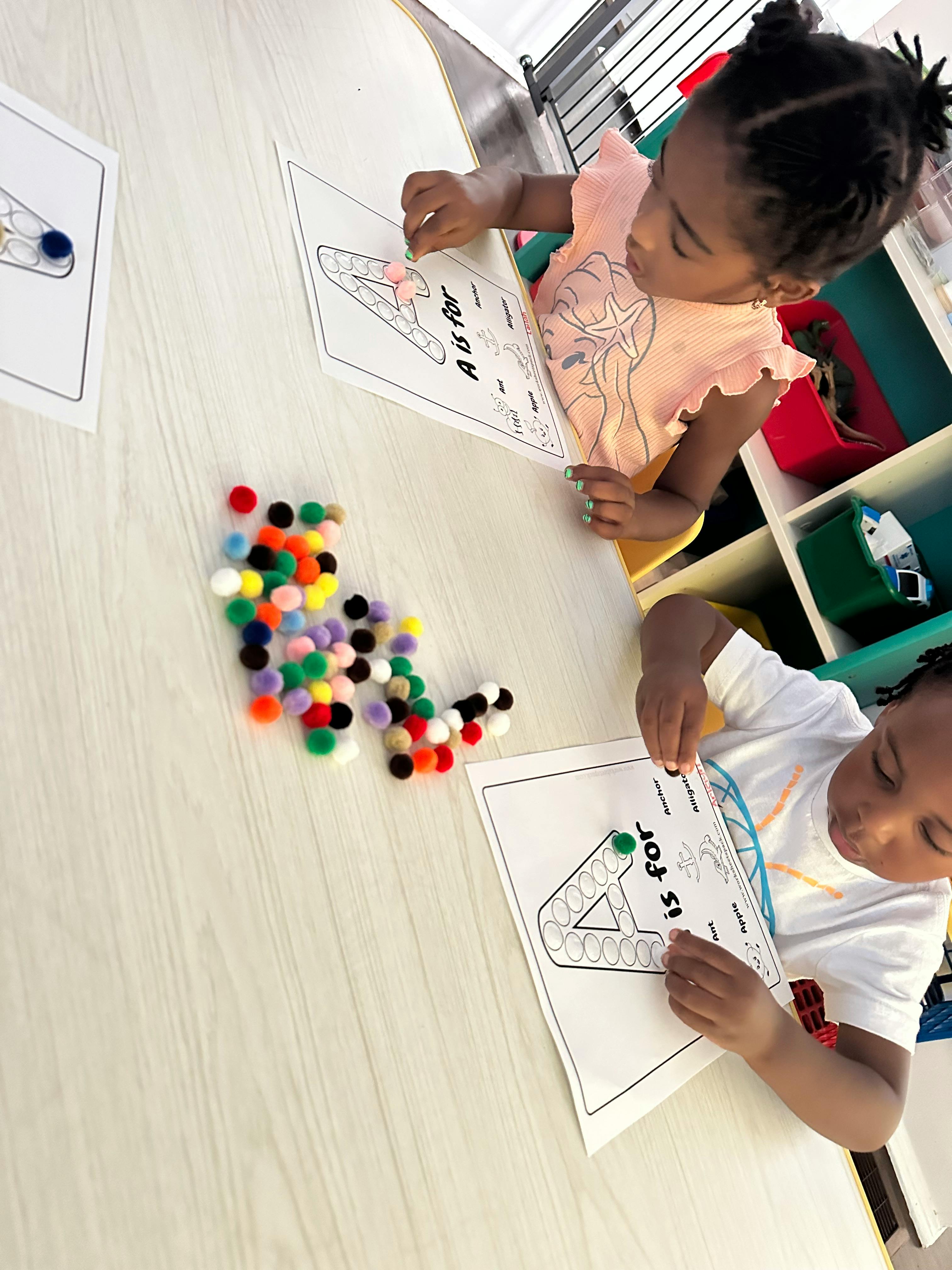 Two children doing an activity with pom-poms and paper with "A is for"