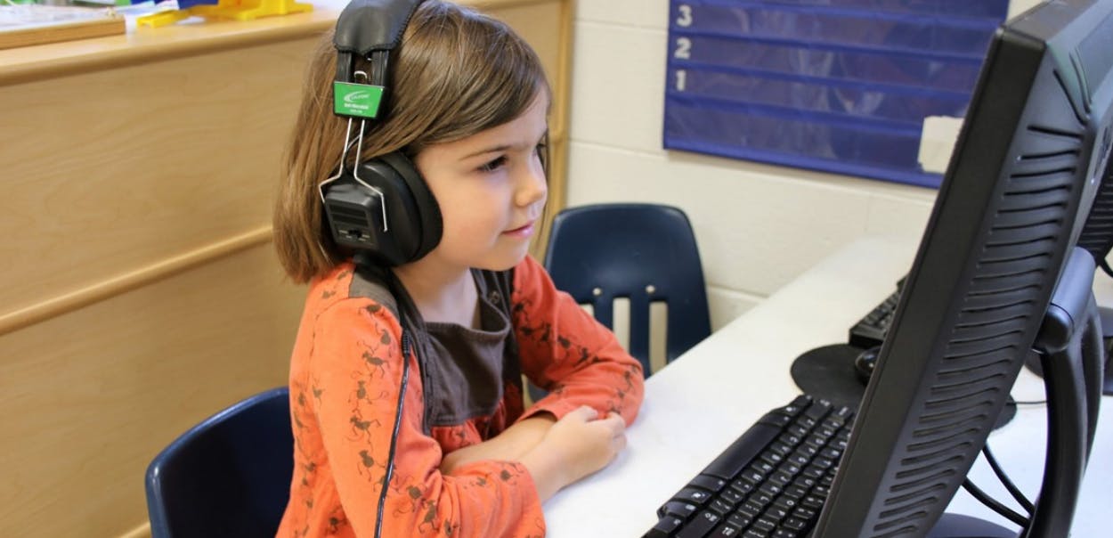 Child wearing headphones looking at a computer screen in a classroom