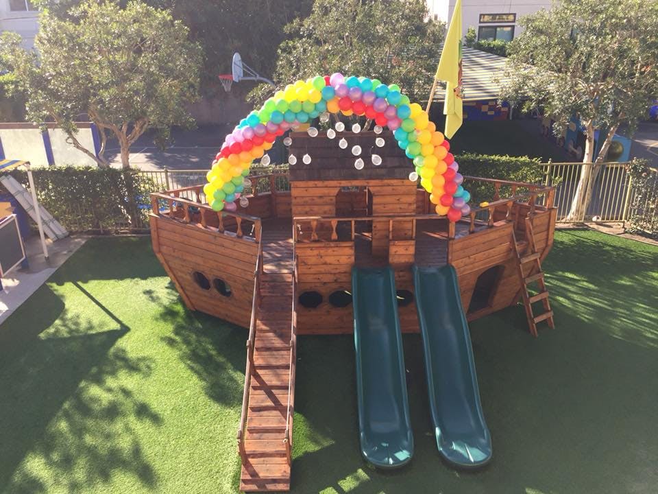Playground with a wooden ship structure, slides, and a balloon arch