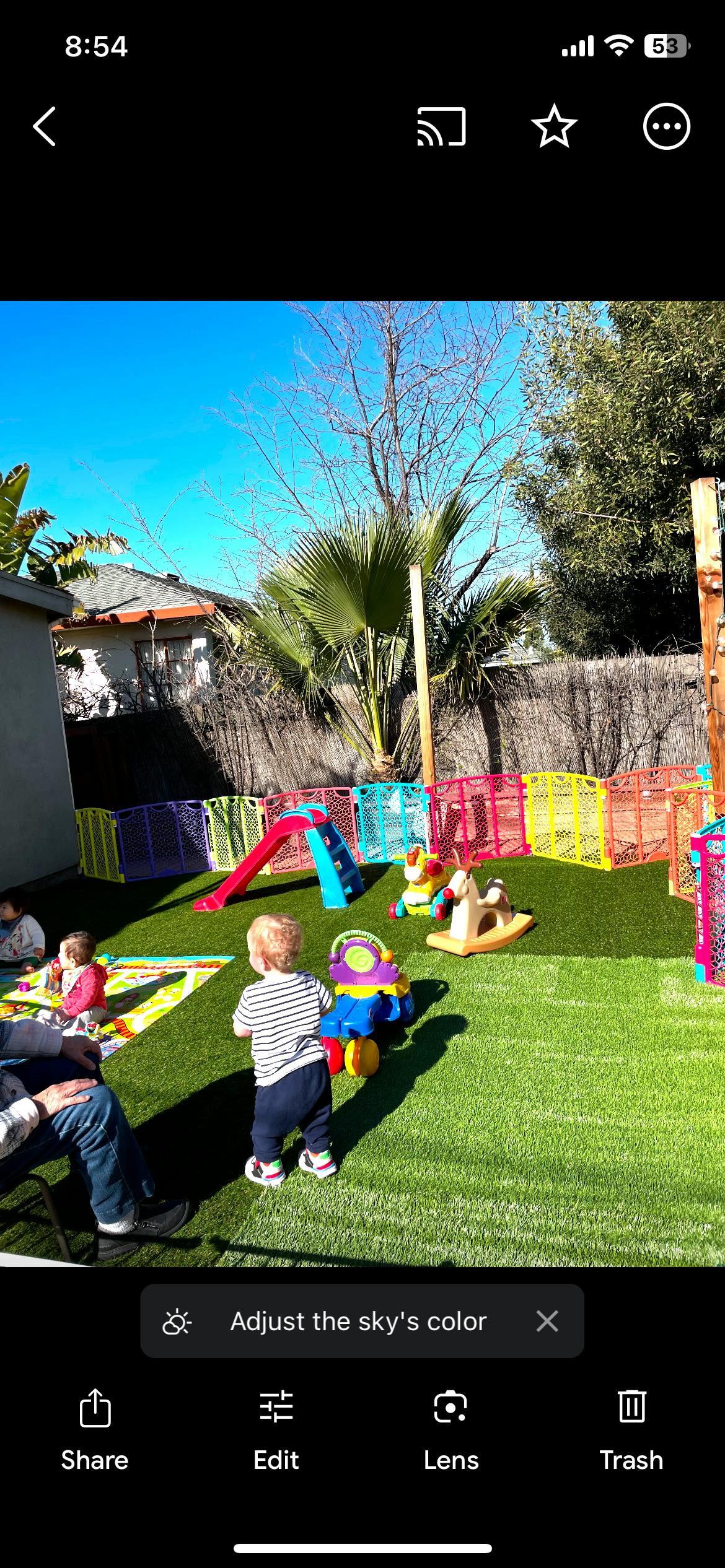 Child standing on grass next to toys and other children in a backyard