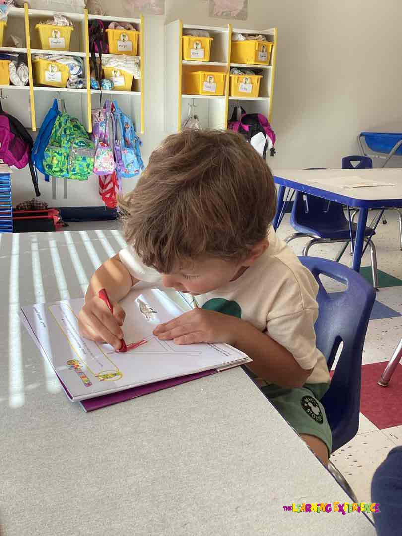 Child drawing on paper at a desk in a classroom