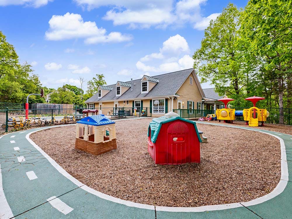 Playground with small playhouses, slides, and tricycles on a wood chip surface