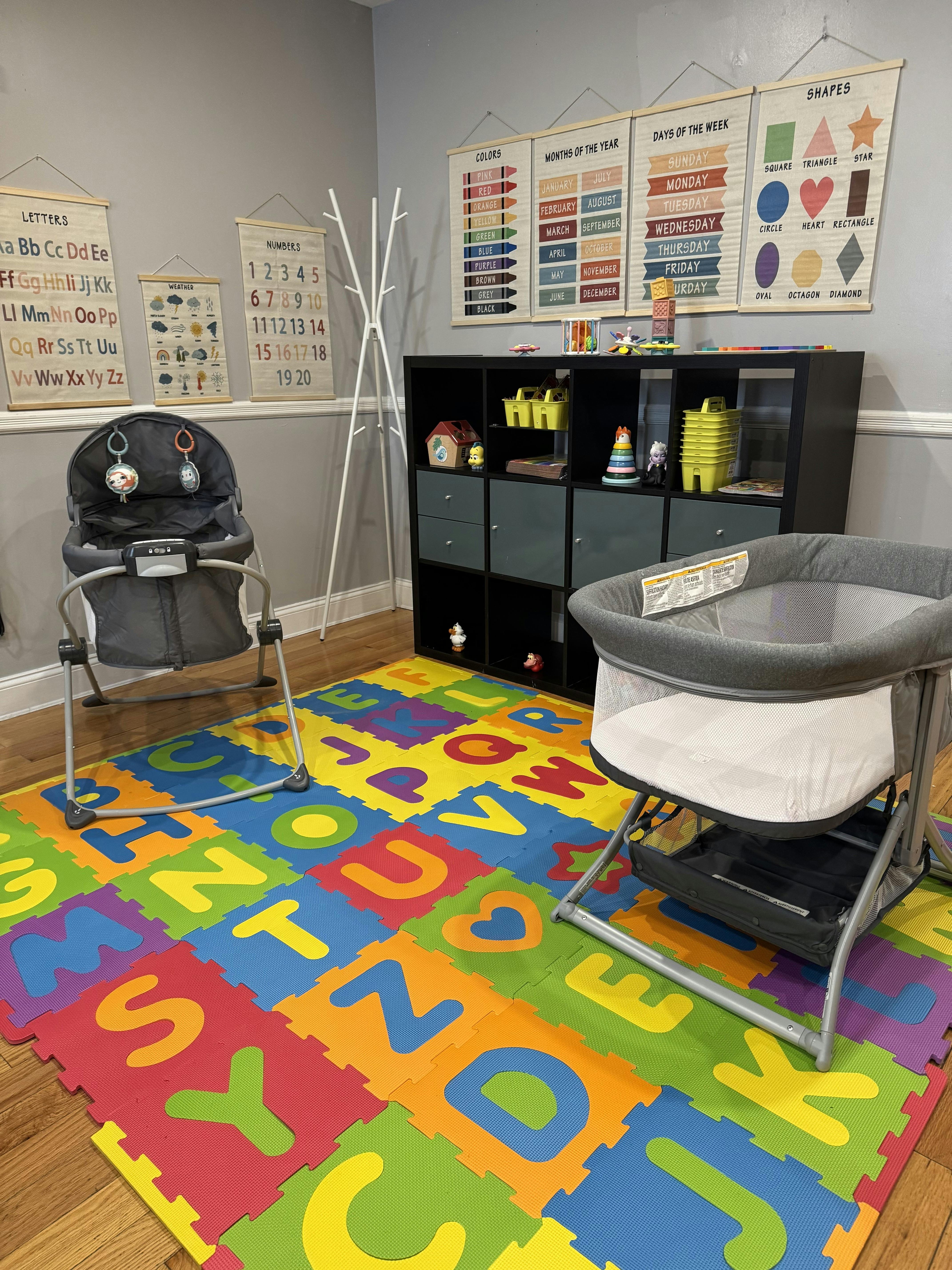Child's play area with alphabet mat, bouncer, bassinet, and storage shelves