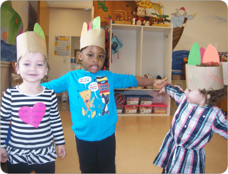 Three children wearing paper crowns in a classroom