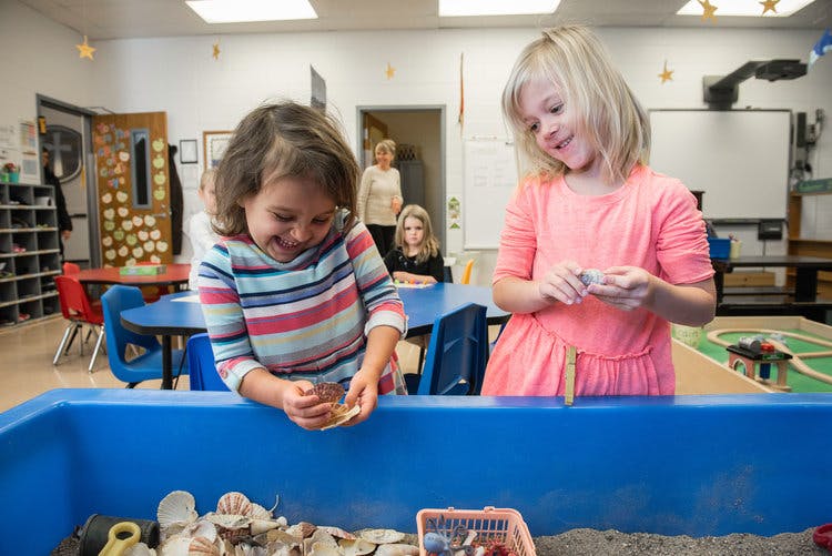 Two children playing in a sand table in a classroom