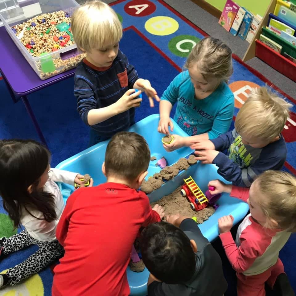 Children playing with sand in a blue sensory bin