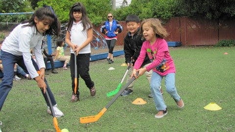 Children playing with hockey sticks on a grassy field