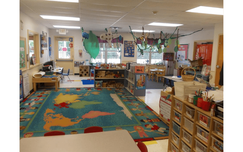 Classroom with a large world map rug, tables, chairs, and shelves of learning materials