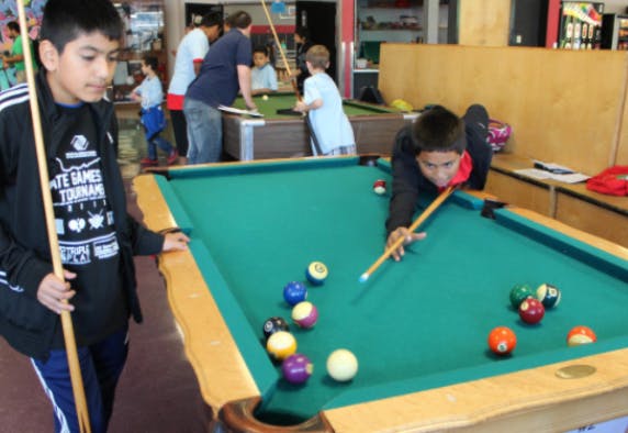 Two children playing billiards, one lining up a shot