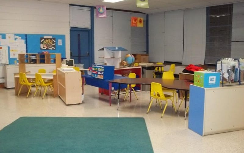Classroom with small tables and yellow chairs, bulletin boards, and learning materials