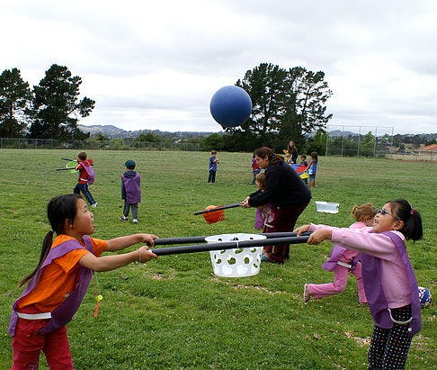 Children playing with a large blue balloon and other toys in a grassy field