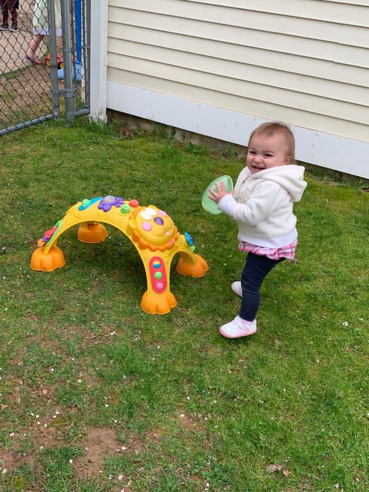 Child standing next to a colorful play tunnel, holding a green object