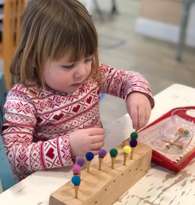 Child playing with a wooden pegboard and colorful pom-poms