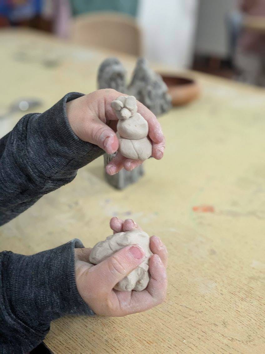 Child's hands holding a small clay sculpture and a lump of clay
