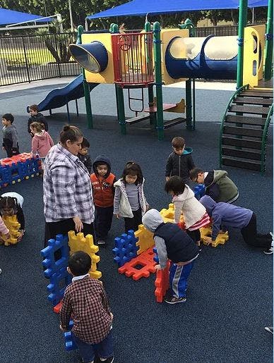 Adult and children playing with large interlocking blocks on a playground
