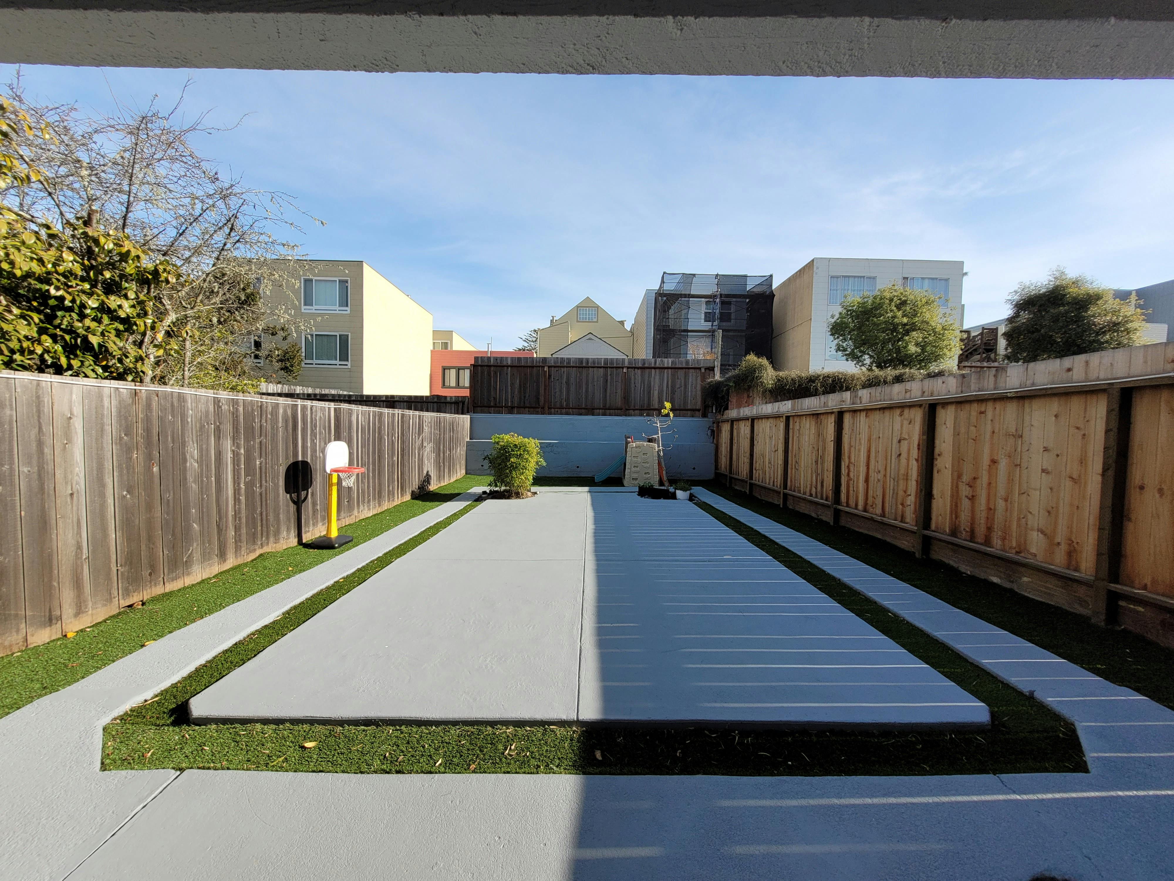 Backyard with concrete paths and artificial turf, surrounded by wooden fences