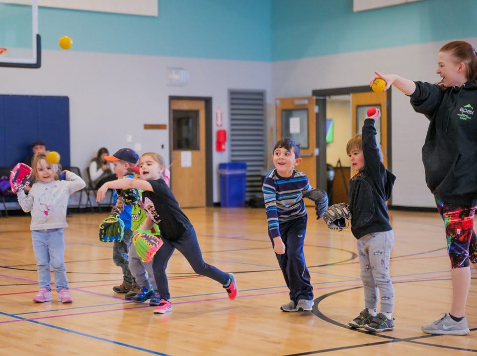 Children and an adult playing with balls and gloves in a gym
