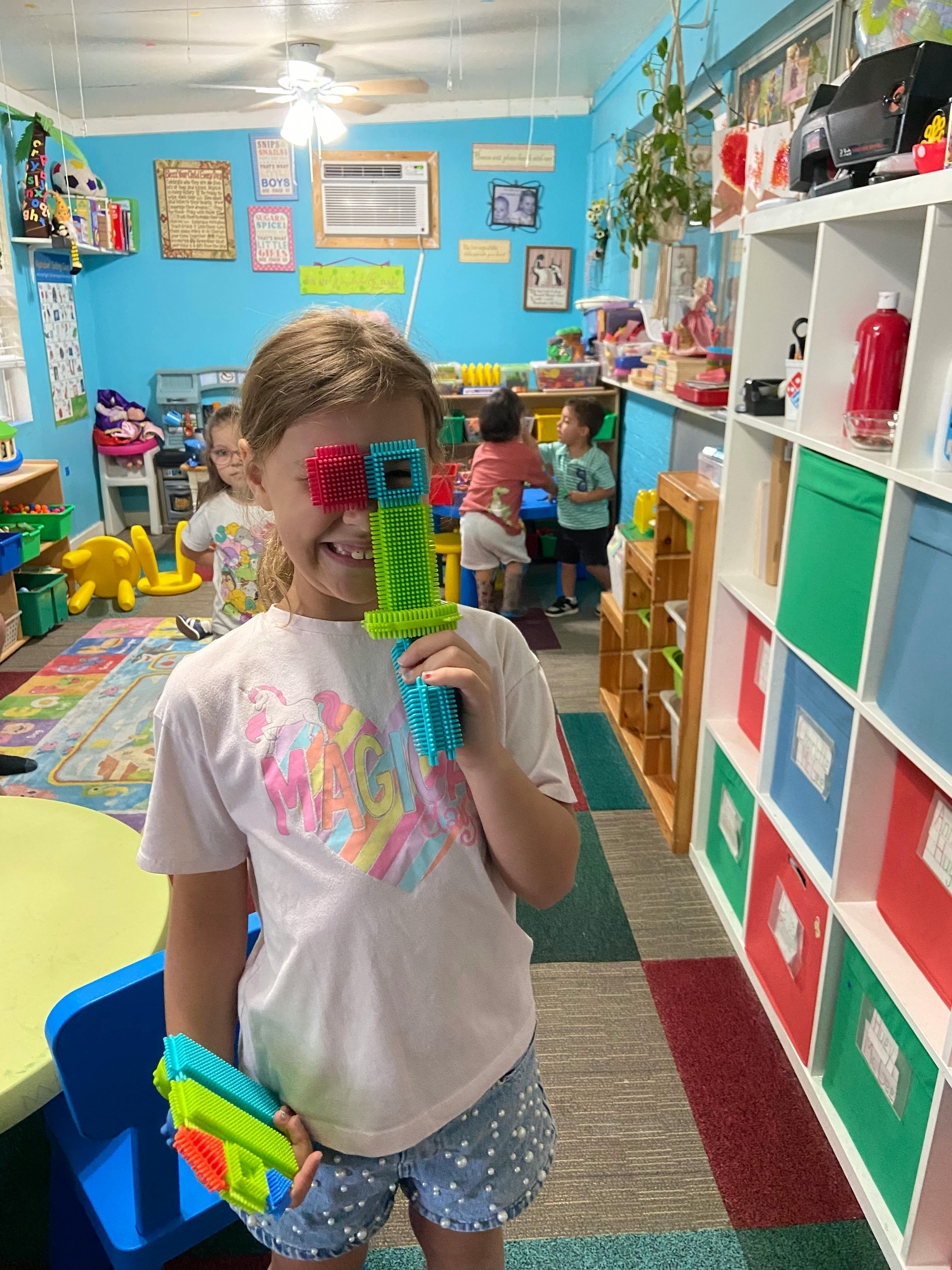 Child smiling while holding colorful interlocking blocks to their face