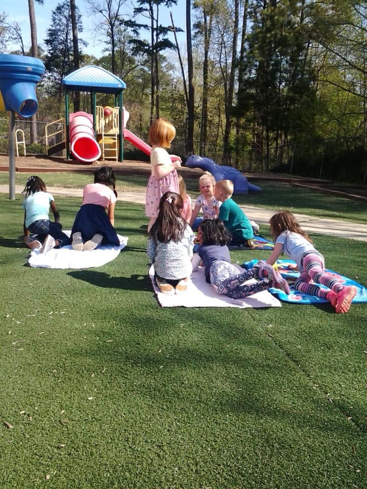 Children sitting and lying on blankets on grass at a playground