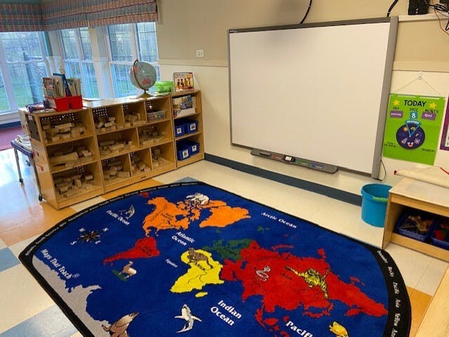 classroom with block storage shelves, interactive whiteboard, and world map rug
