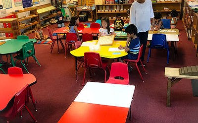 Children and an adult in a classroom with colorful tables and chairs
