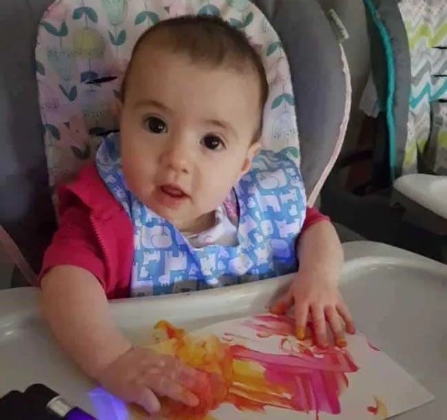 Child in a high chair with a bib, playing with paint on paper
