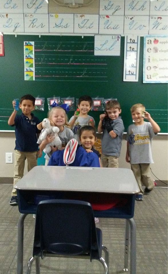 Six children standing in a classroom with a desk in the foreground