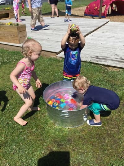 Three children playing with toys in a metal tub of water outdoors
