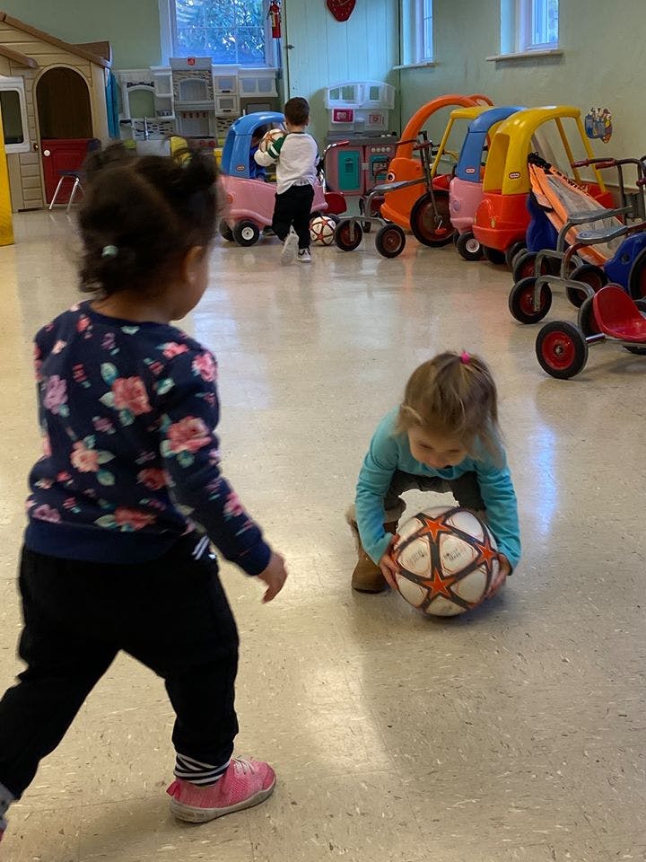 Child playing with a ball on the floor, another child standing nearby