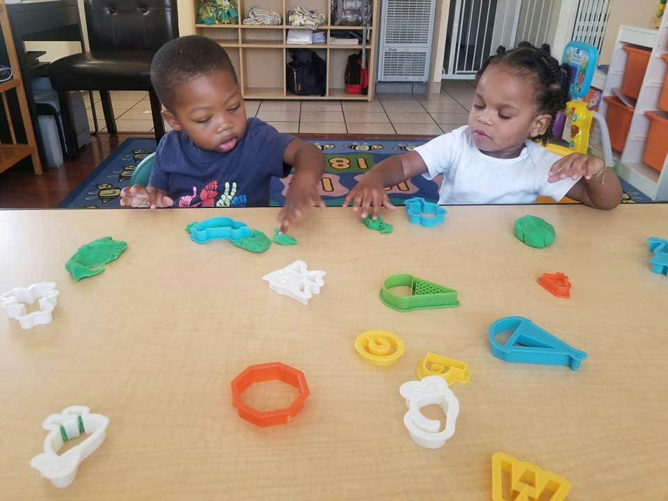 Two children playing with colorful playdough cutters on a table